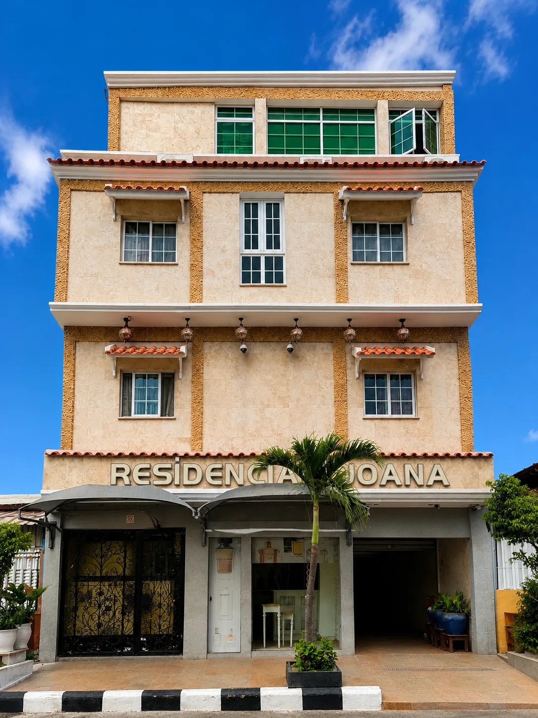 Fachada de três pisos Residencial Joana com o letreiro em relevo sobre a entrada e uma palmeira no passeio